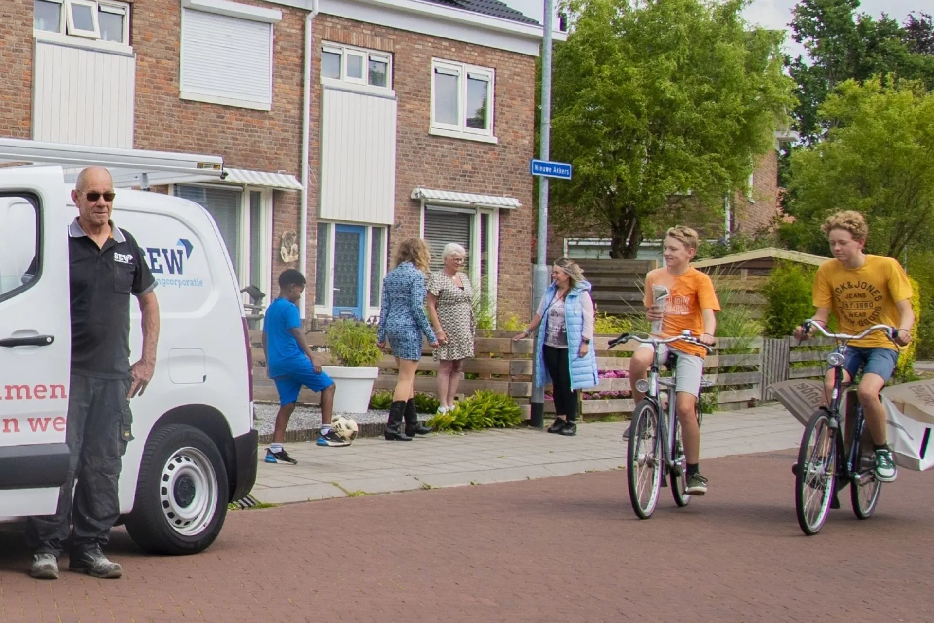 Twee mensen fietsen langs een geparkeerde SEW bestelwagen in een woonwijk.